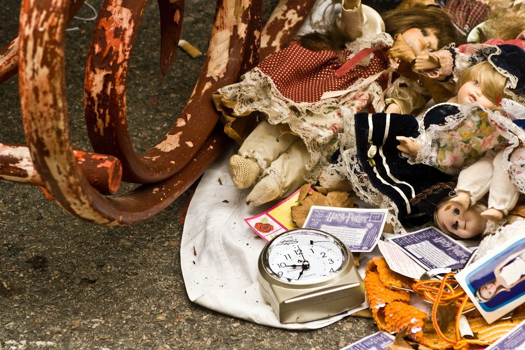 Déchets déversés au sol : des poupées, un réveil, des papiers et une structure en métal rouillé